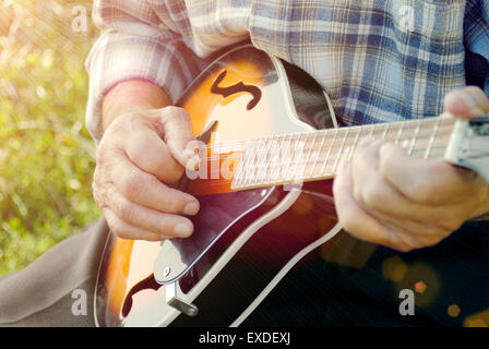 Senior man playing mandolin outside on the green background Stock Photo