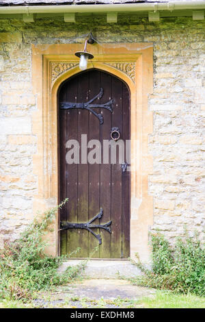 England, Quenington. Norman period, circa 1100, Christian Church, St Swithin's, side wooden door with ornate carvings over the top and light. Stock Photo