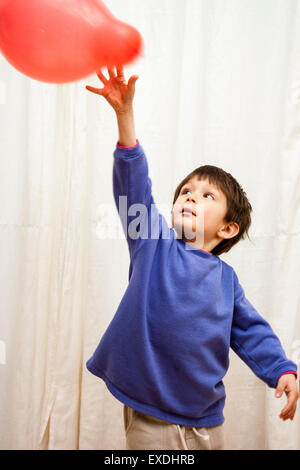 Caucasian child, boy, playing indoors with colored balloons. 6-7 year old enjoying hitting floating balloons against a background of white curtains.