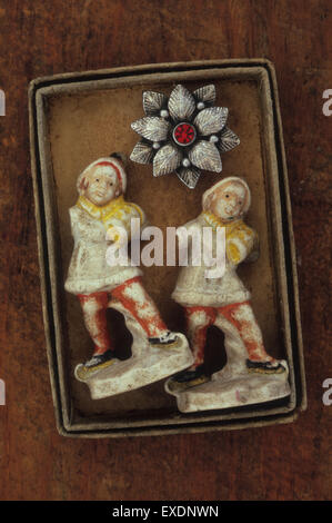 Two identical vintage ornamental figures carrying barrels of water each with broken arm lying in box with silver brooch Stock Photo