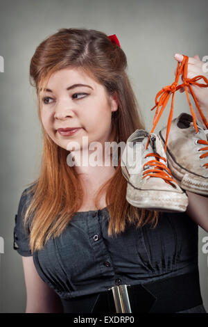 Cute girl holds up two smelly stinky sneaker shoes Stock Photo