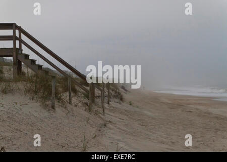 A misty, hazy weather beach scene with a wooden stairway leading down to the sand with a distant walker Stock Photo