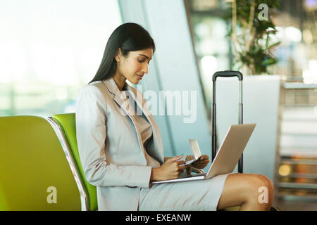 pretty Indian businesswoman checking flight information on laptop computer at airport Stock Photo