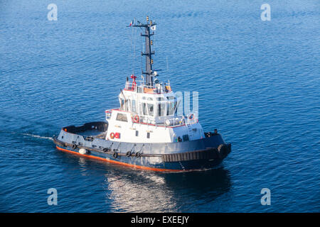 Tug boat with white superstructure and dark blue hull underway on sea water Stock Photo
