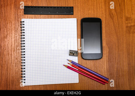 Pencils, pencil sharpener, ruler and mobile phone lying on notebook. Blank sheets of paper. Back to school. Stock Photo