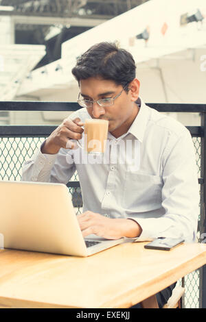Asian Indian businessman using laptop computer while drinking a cup hot milk tea. Stock Photo