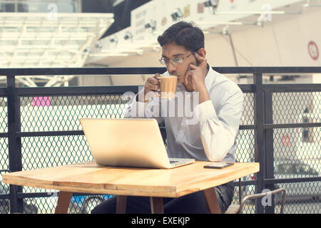 Asian Indian businessman using laptop computer while drinking a cup hot milk tea. Stock Photo