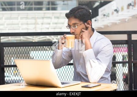 Asian Indian businessman using laptop computer while drinking a cup hot milk tea. Stock Photo