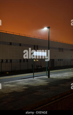 An empty deserted railway station with a blank location sign at night in the mist fog UK Stock Photo