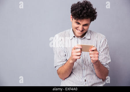 Smiling young man playing on smartphone over gray background Stock Photo