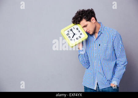 Tired man holding big clock over gray background Stock Photo