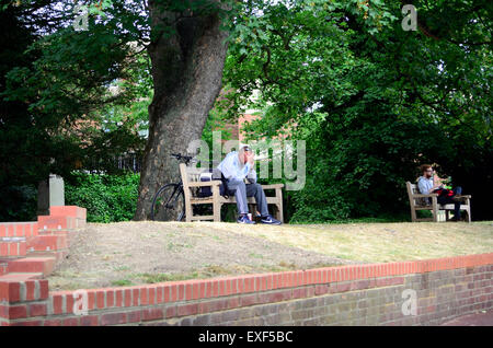 A man sits on a park bench with his head in his hand while on a mobile phone call. His bicycle is propped up behind him and his Stock Photo