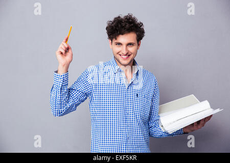 Happy casual man holding pencil and folder with files over gray background. Looking at camera Stock Photo
