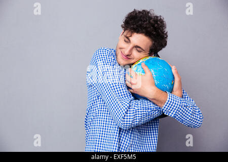 Happy young man hugging globe over gray background Stock Photo