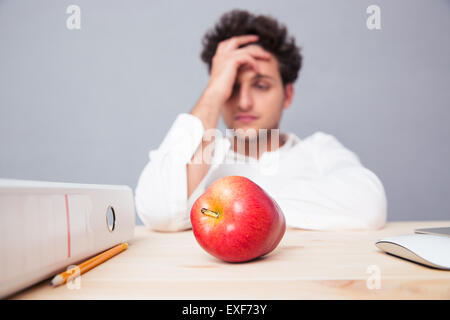 Young pensive businessman sitting at the table with folder and red apple. Focus on apple Stock Photo