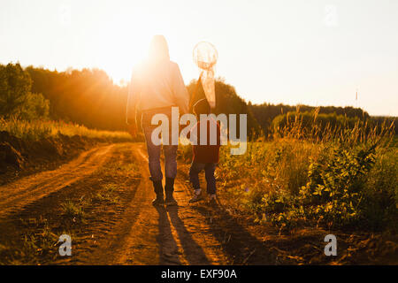 Rear view of father and son with butterfly net walking along dirt track at sunset, Sarsy village, Sverdlovsk Region, Russia Stock Photo