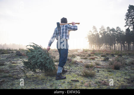 Mature woodsman walking in forest clearing with axe over his shoulder Stock Photo