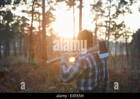 Rear view of woodsman with axe over his shoulder in forest at sunset Stock Photo