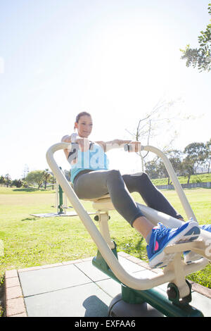 Mid adult woman in park training on rowing machine Stock Photo