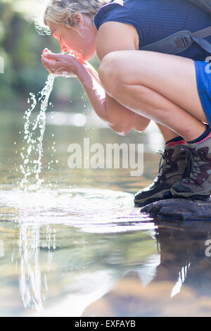 Hiker washing face with water from shallow stream Stock Photo