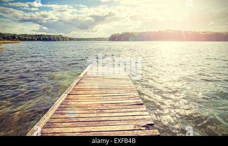 Retro style old wooden pier with flare effect at sunset. Stock Photo