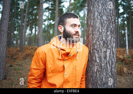Young man leaning against tree looking out from forest Stock Photo