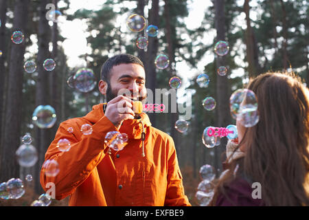 Young couple blowing bubbles together in forest