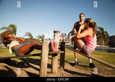 Two young women doing sit ups on wooden workbench in  park Stock Photo