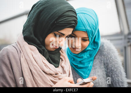 Two young female friends reading smartphone texts on park path Stock Photo