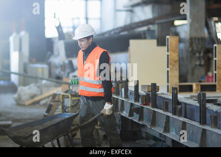 Factory worker pushing wheelbarrow in concrete reinforcement factory Stock Photo