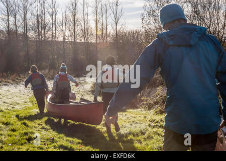 Four people carrying canoe across grass Stock Photo