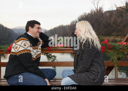 Heterosexual couple sitting face to face on bench, beside lake, Lombardy, Italy Stock Photo