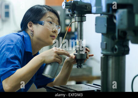 Young woman using drill in industrial workshop Stock Photo