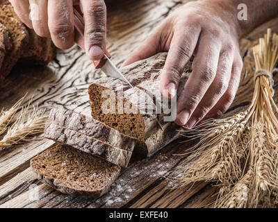 Man's hands cutting bread on the wooden plank. Stock Photo