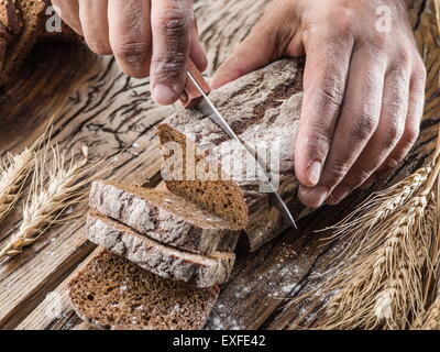Man's hands sliced bread on the old wooden plank. Stock Photo
