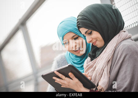 Two young women wearing hijabs using digital tablet on footbridge Stock Photo