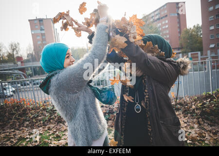 Two young women in park play fighting with autumn leaves Stock Photo