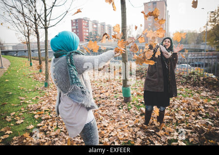 Two young women play fighting with autumn leaves in park Stock Photo