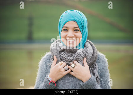 Portrait of young woman in park wearing turquoise hijab Stock Photo