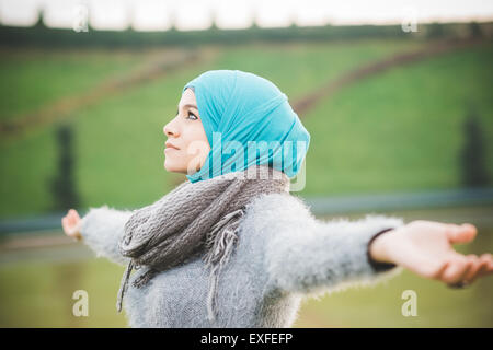 Young woman in park with arms open wearing turquoise hijab Stock Photo