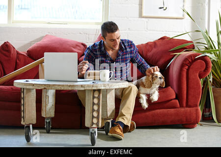 Mid adult man writing address on parcels whilst petting dog in picture framers Stock Photo