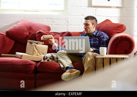 Mid adult man preparing parcels on sofa in picture framers showroom Stock Photo