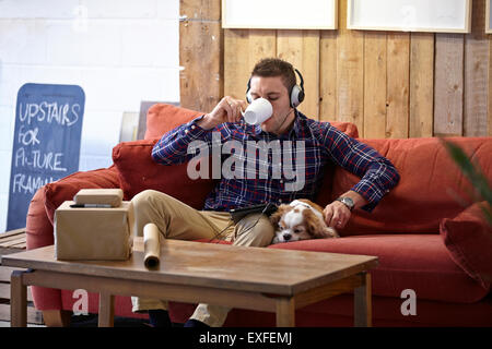 Mid adult man drinking coffee and petting dog in picture framers showroom Stock Photo