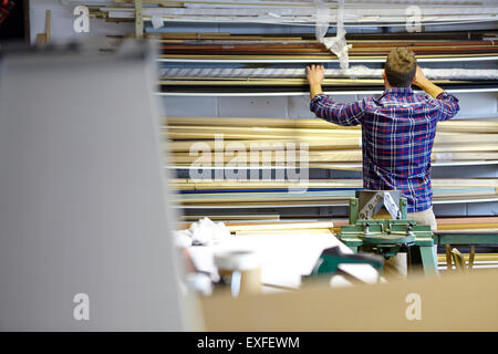 Rear view of man searching stockroom shelves in picture framers workshop