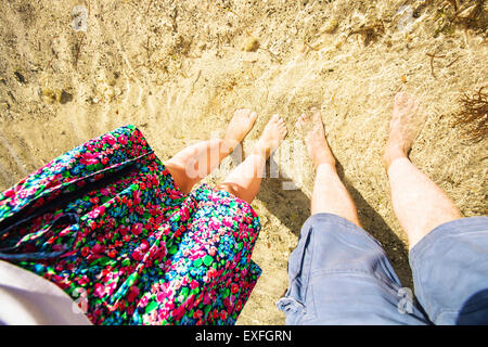 Male and feemale legs standing in shallow water seen from above. Selfie Stock Photo