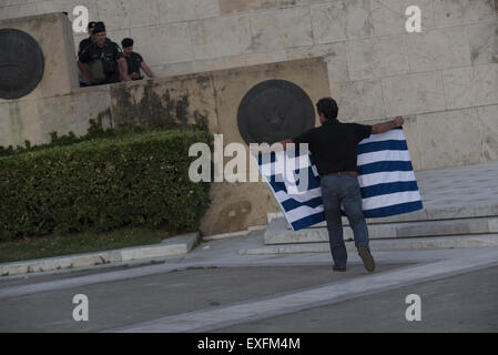 Athens, Greece. 13th July, 2015. A protester holds a Greek flag. Hundreds gathered at Syntagma square in front of the Greek perliament to protest against the bailout deal primeminister A. Tsipras agreed to at the Euro Summit. Credit:  Nikolas Georgiou/ZUMA Wire/ZUMAPRESS.com/Alamy Live News Stock Photo