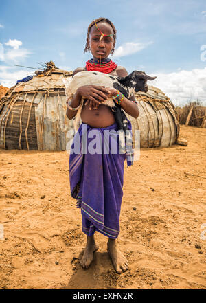 Girl from the African tribe Dasanesh holding a goat in her village Stock Photo