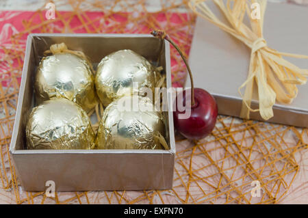 Chocolate candies wrapped in golden coloured packaging in a red present box with fresh cherries Stock Photo