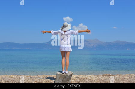 Young woman looking at the mountains above sea with her arms wide open on a sunny summer day Stock Photo