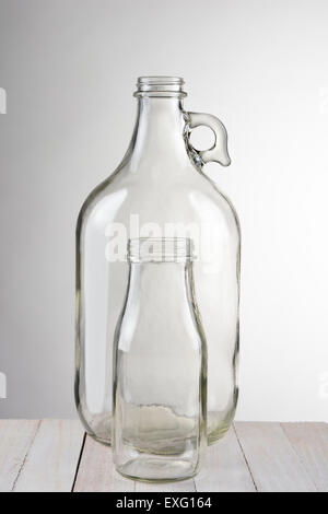 Two empty glass bottles, a small bottle in front of a larger container. Vertical format against a light to dark gray background. Stock Photo